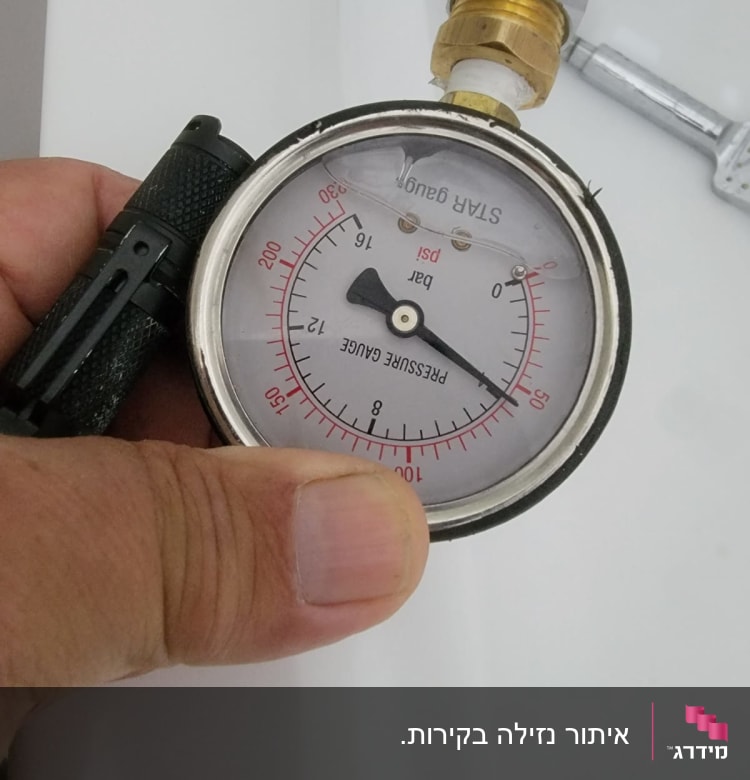 מד לחץ מחובר לצינור, יד מחזיקה את המכשיר